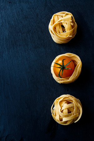 Dry pasta and fresh cherry tomato over dark gray background. Copy space. Top view.の写真素材