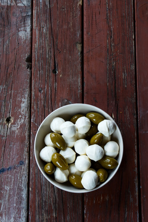 green olives and mozzarella cheese in ceramic bowl on rustic wooden background, top viewの写真素材