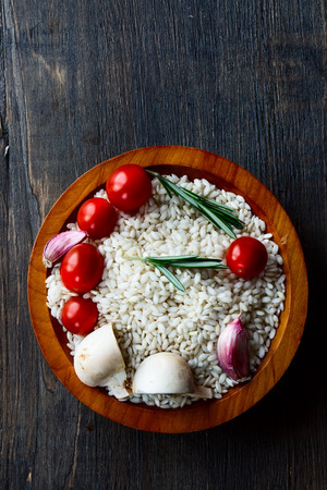 Rice with raw vegetable for cooking in bowl on dark rustic wood texture, top viewの写真素材