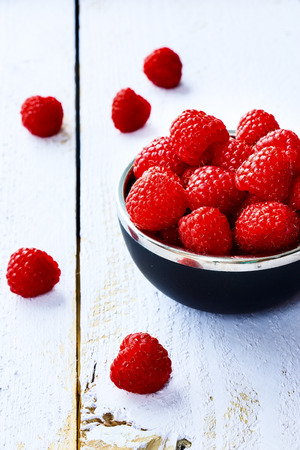 Raspberry in bowl on white wooden board. Selective focus.の写真素材