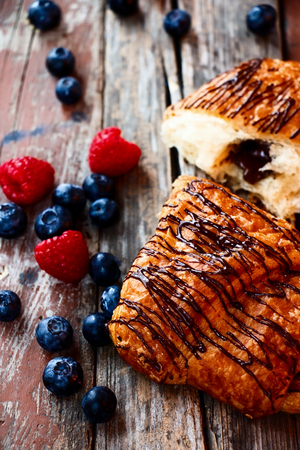 freshly baked chocolate croissants with berries for breakfast over rustic wooden texture. Selective focus.の写真素材