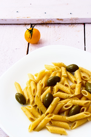 Penne pasta with pesto, olives and tomatoes on white wooden background.の写真素材