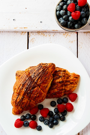 Top view of plate with chocolate croissants with berries on white wooden background.の写真素材