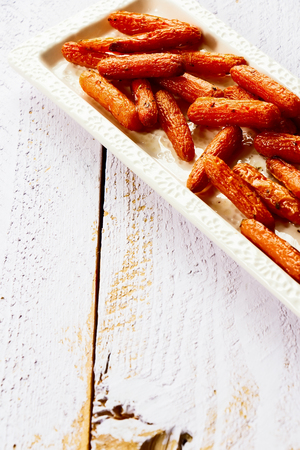 Baked baby carrots with oregano on white wooden background. Selective focus.の写真素材