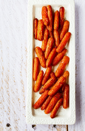 Top view of roasted baby carrots over wooden white background.の写真素材