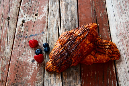 Fresh chocolate croissants with berries for breakfast over rustiv wooden background.の写真素材
