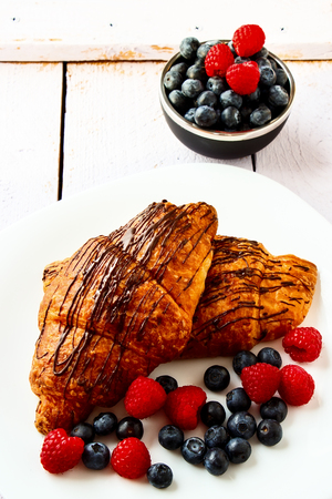 Breakfast with chocolate croissants with berries on plate over white wooden background.の写真素材