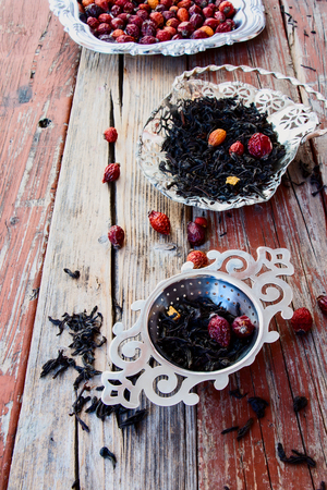 Hip roses and tea leaves on rustic wooden table.の写真素材
