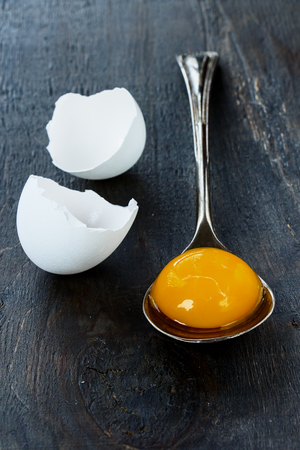 Raw egg on vintage spoon with eggshell over dark background. Selective focus.の写真素材
