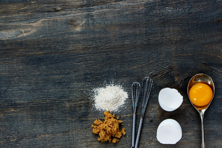 Rustic background with flour, brown sugar, yolk in spoon on dark wood table. Top view. Free text spaceの写真素材