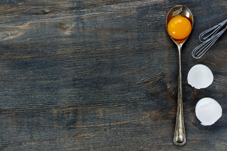 Baking background with egg yolk in vintage spoon and eggshell over dark wooden texture. Top view.の写真素材