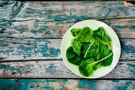 Spinach leaves in plate over rustic wooden texture. Top view.の写真素材
