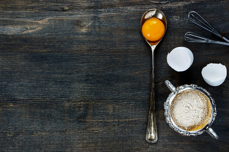 Food background with copy space - egg yolk in vintage spoon and flour in vintage cup on wooden texture. Top view.の写真素材