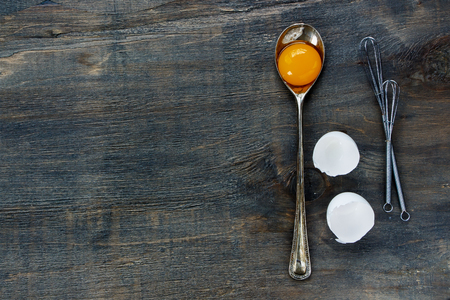 Cooking background with egg yolk in vintage spoon and eggshell over dark wooden texture. Top view.の写真素材