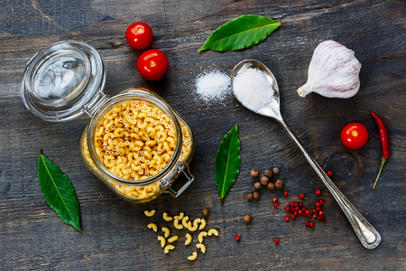 Italian pasta in glass jar, tomatoes and spices over dark wooden background. Top view.の写真素材