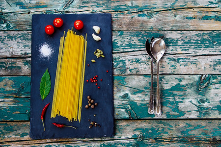Top view of vintage spoon and ingredients for cooking italian pasta over wooden and slate background.の写真素材