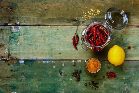 Hot Chili Peppers in glass jar with herbs and spices over rustic wooden board - cooking or spicy food concept. Background with space for text.の写真素材