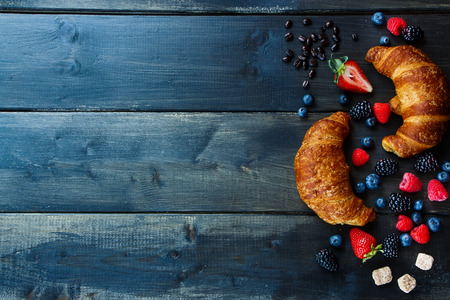 Top view of coffee, berries and fresh croissants for breakfast over wood. Background with space for text.の写真素材
