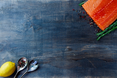 Delicious salmon fillet, aromatic spices and lemon on dark wooden background with space for text. Vegetarian food, health or cooking concept. Top view.の写真素材