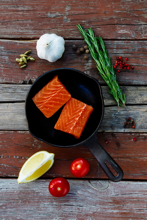 Red fish on vintage cast iron skillet with ingredients over rustic wooden background. Vegetarian food, health or cooking concept.の写真素材