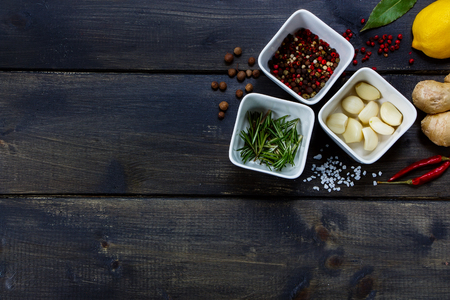 Top view of ceramic bowls with fresh herbs and spices ( garlic, pepper, rosemary) on rustic wooden background with sample text.の写真素材