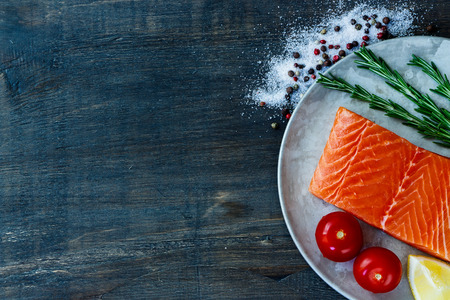Portion of raw salmon on old metal plate with rosemary and aromatic spices. Seafood on dark wooden background with space for text. Vegetarian food, health or cooking concept.の写真素材