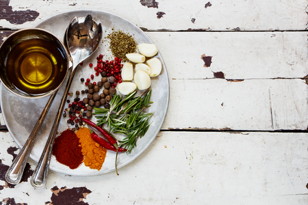 Olive oil, fresh herbs and spices on vintage metal plate over white rustic background. Top view, place for text.の写真素材