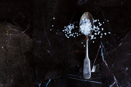 Sea salt in old metal spoon on a stone background with space for text. Top view. Cooking, healthy eating.の写真素材