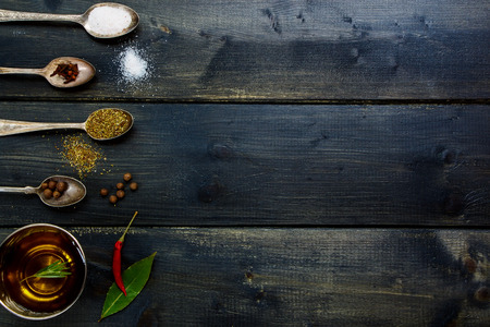 Ingredients - olive oil, herbs and spices, old metal spoons and dark wooden background - cooking, healthy eating. Top view.の写真素材
