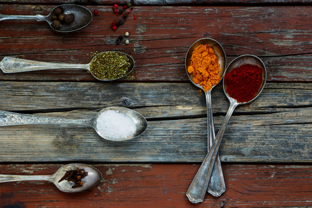 Old metal spoons with herbs and spices selection on rustic wooden background, close up, top view. Cooking concept.の写真素材