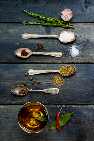 Top view of olive oil, herbs and spices, old metal spoons and dark wooden background - cooking, healthy eating. Top view.の写真素材