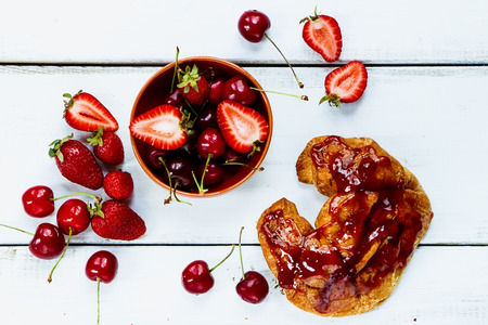 Fresh strawberries and cherries with croissant on white wooden background.の写真素材