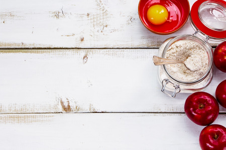 Ingredients for apple pie cooking. Fresh red apple, eggs, flour in jar on a rustic wooden background.の写真素材