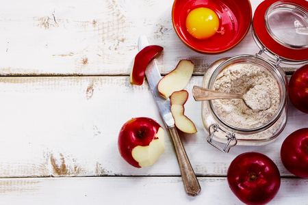 Ingredients (fresh red apples, eggs, flour in jar) on white wooden background for apple pie cooking.の写真素材