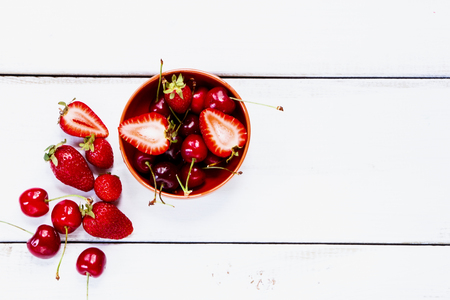 Bowl with freshly picked strawberries and cherries on white wooden background.の写真素材