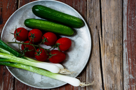 Vegetables (cucumbers, tomatoes and green onion) on old metal plate. Healthy eating concept.の写真素材