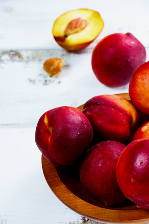 Juicy peaches in wooden bowl over white background. Selective focus.の写真素材
