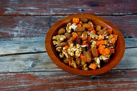 Assorted dried fruits and nuts mix in a wooden bowl on rustic background.