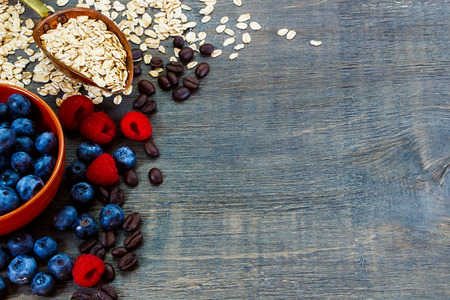 Coffee beans, oat flake in vintage scoop and fresh berries in bowl on dark wooden background with space for text. Health and diet concept.の写真素材
