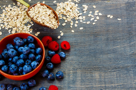 Oat flake in vintage scoop and fresh berries in bowl over wood. Background with space for text. Health and diet concept.の写真素材