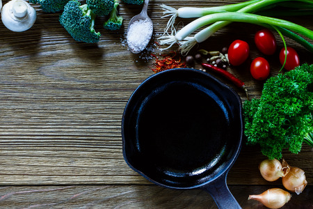 Cooking background with fresh ingredients and iron pan over rustic wood. Vegetarian food, health or cooking concept. Top view. Free space for text.の写真素材