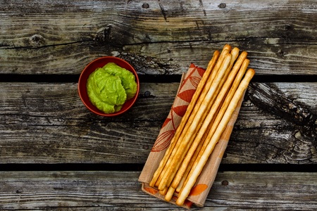 Healthy snack. Fresh guacamole dip with bread sticks over rustic wooden background with space for text. Top view.の写真素材