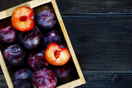 Close up of wooden box with plums over old dark board. Top view. Fruits background with space for...