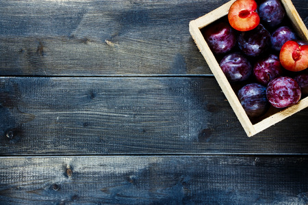 Top view of wooden box with plums over old dark board. Fruits background with space for text. Agriculture, Gardening, Harvest Concept.の写真素材