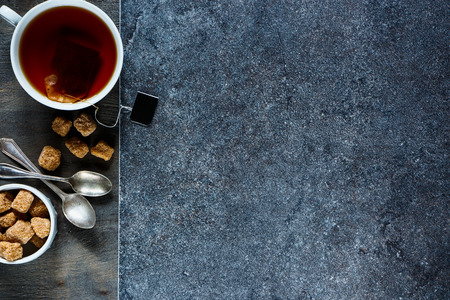 Close up of tea cup with teabag and brown sugar over stone and vintage wooden texture. Dark background layout with free text space. Top view.の写真素材
