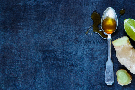Honey in old metal spoon, lemon and ginger on dark vintage background. Health concept. Rustic background layout with free text space. Top view.の写真素材