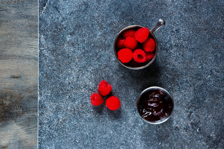 Fresh raspberry in vintage cup and homemade raspberry jam (marmalade) on stone and rustic wooden...