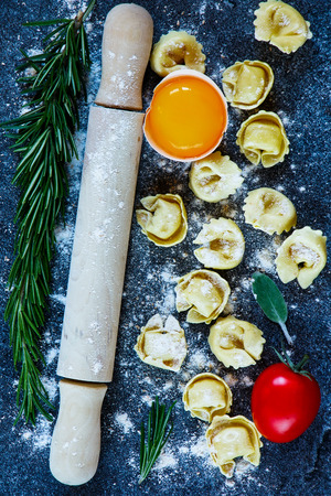 Italian pasta tortellini with tomato, flour, egg and rosemary on dark vintage texture. Top view.の写真素材