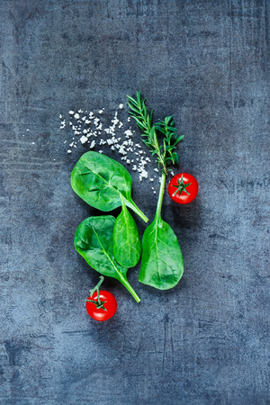 Healthy food background with fresh vegetarian ingredients (spinach, tomatoes, grey salt and herbs) on dark vintage table, top view.の写真素材