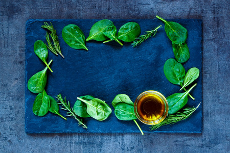 Fresh delicious baby spinach leaves and olive oil on dark slate background, top view.の写真素材